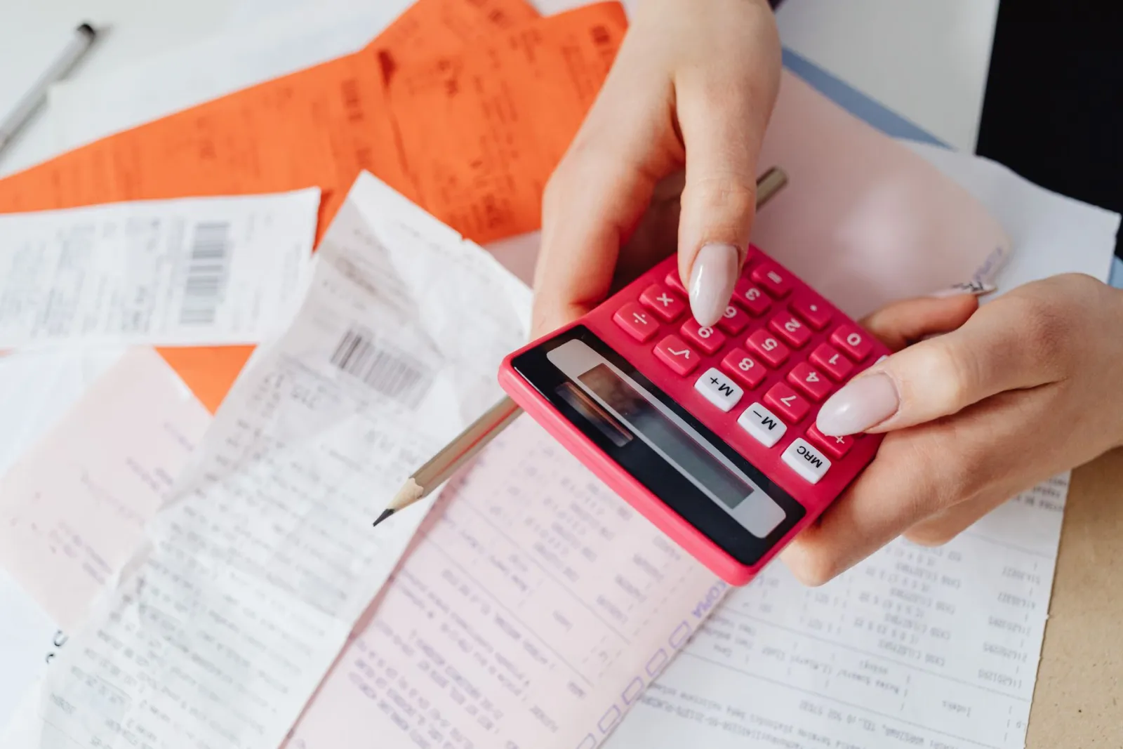 Hands working a calculator over a pile of bills and statements