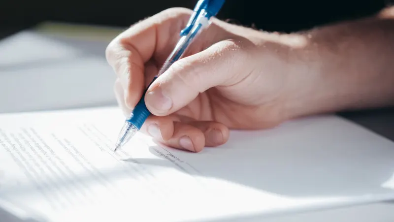 Hand signing a printed agreement with a blue pen