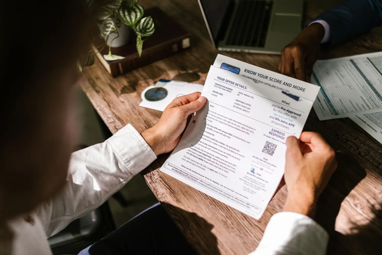 Hands holding a credit offer letter at a desk, reading the fine print