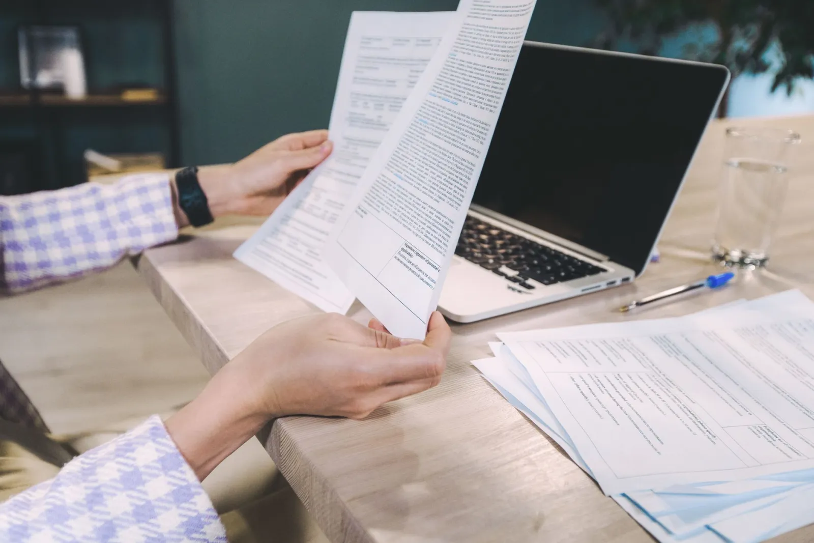 Hands holding a printed report beside an open laptop
