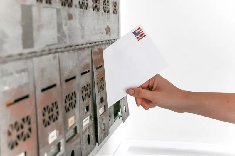 Hand dropping a letter into a wall of mailboxes