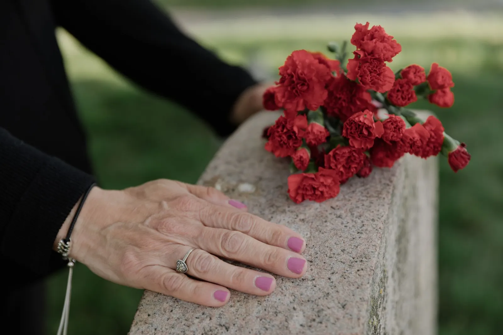 Hand resting on a stone memorial beside red carnations