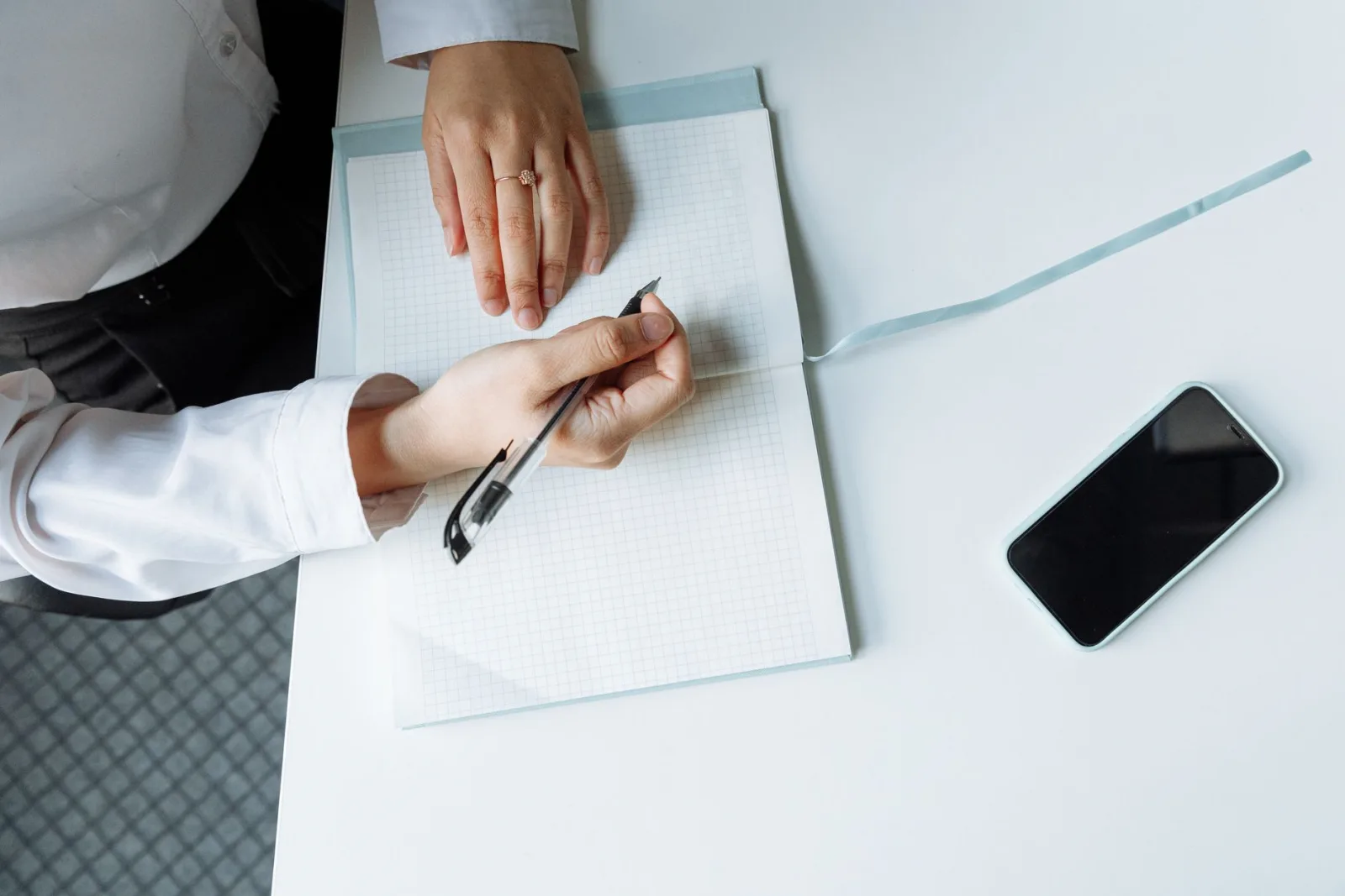 Hands holding a pen over an open notebook on a white desk, ready to take notes