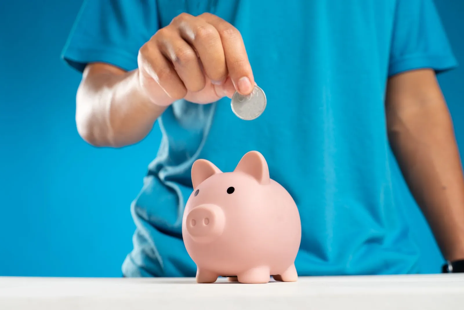 A child dropping a coin into a pink piggy bank