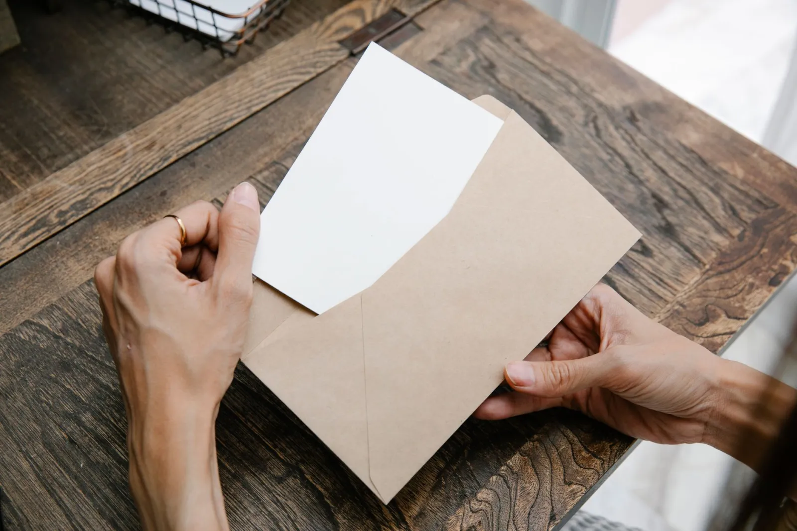 Hands opening a letter from a kraft envelope on a wooden table
