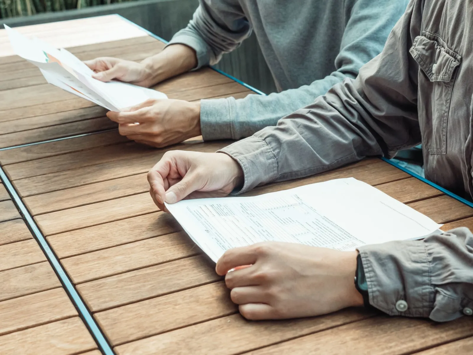 Two people side by side, each holding their own paperwork at one table